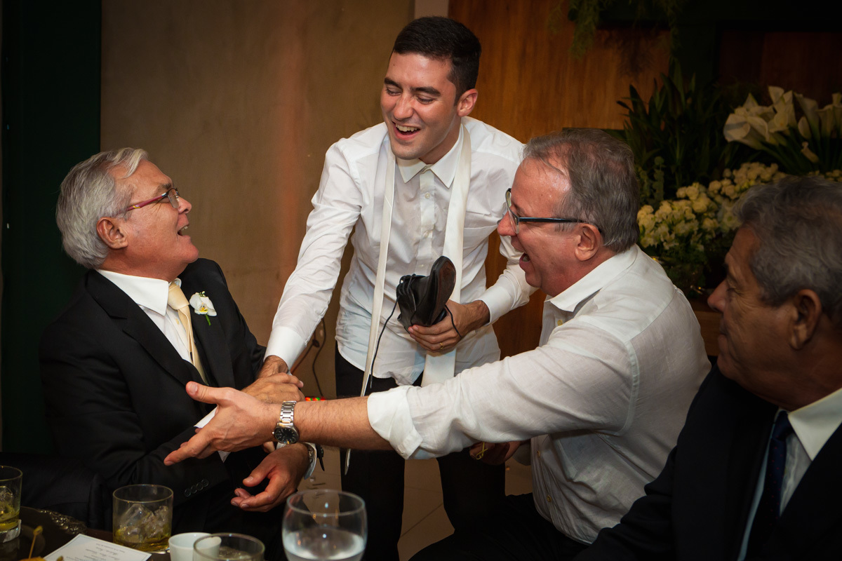 noivo puxando pai e tio na mesa para beber whisky do sapato