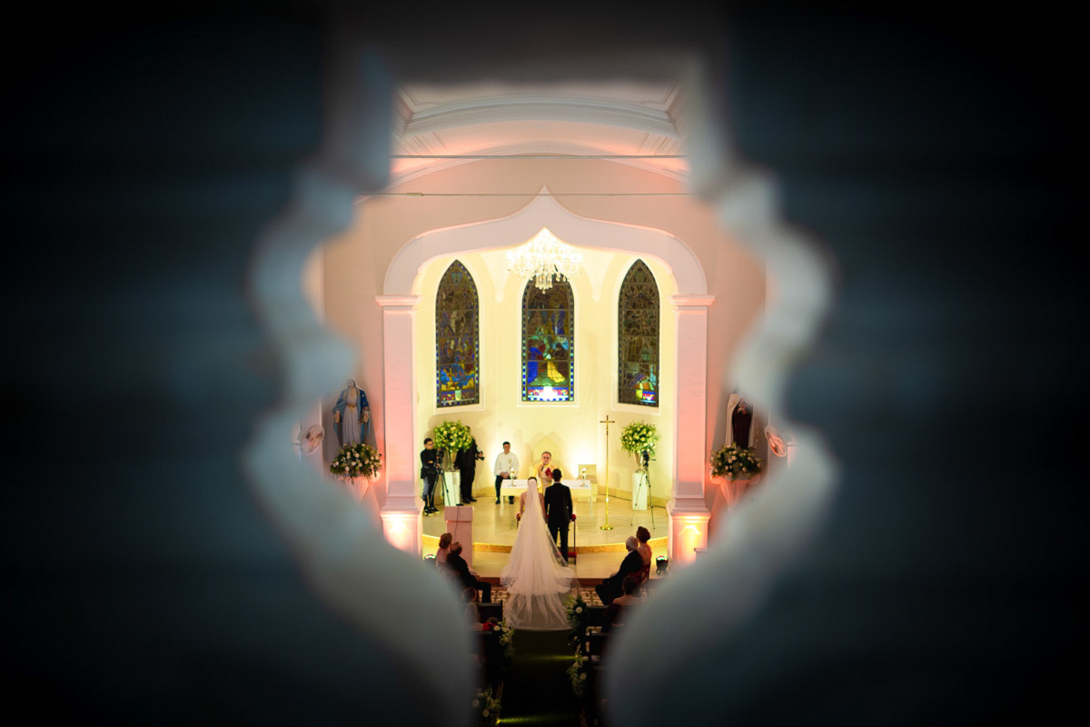 Noivos ajoelhados no altar e foto feita pelo buraco do pergolado