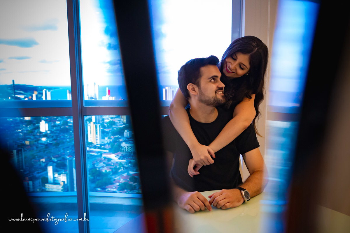 homem sentado na cadeira e namorada abraçando por tras