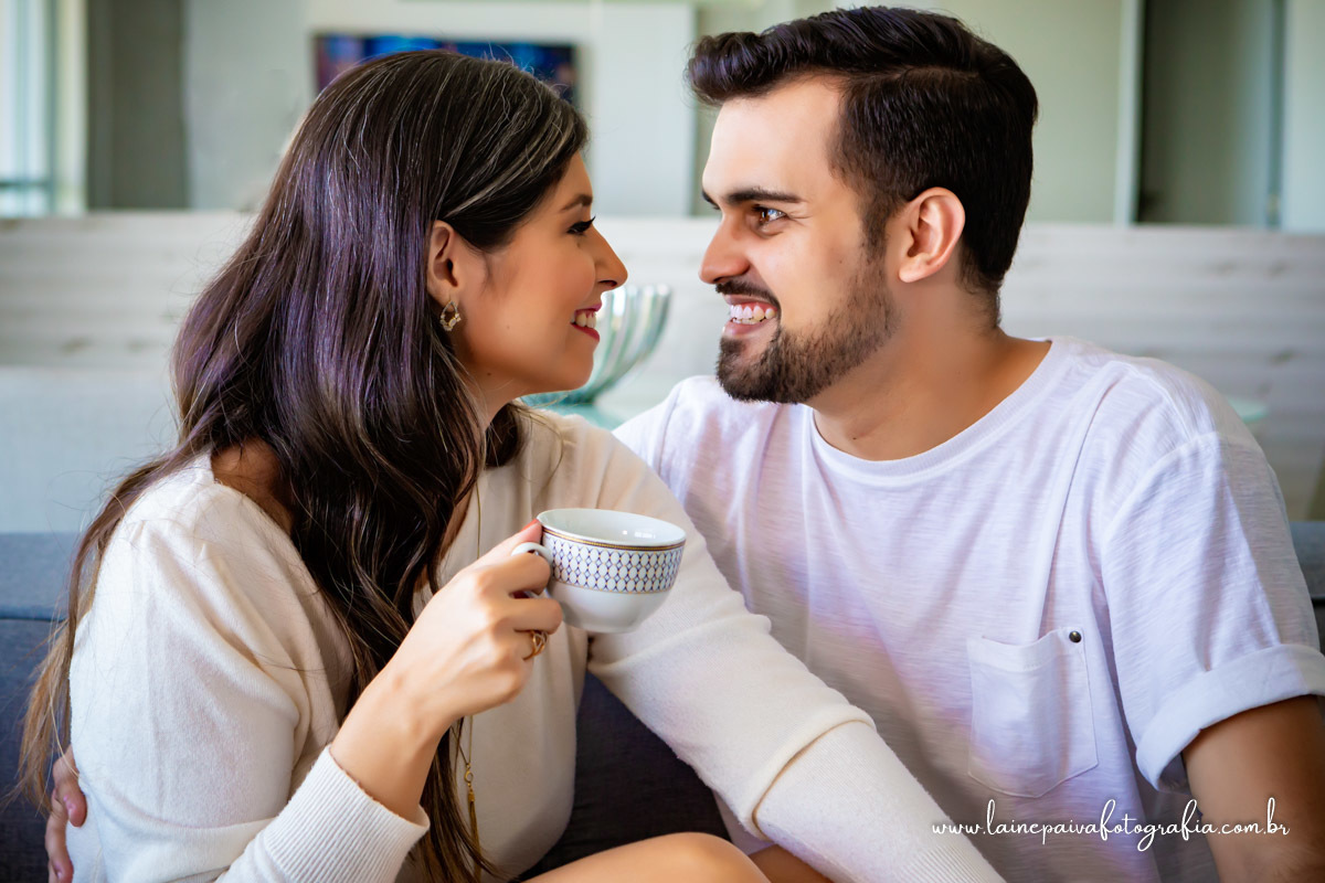 namorados sentados no sofá. Ela segurando uma xicara de cha na mão e se olhando
