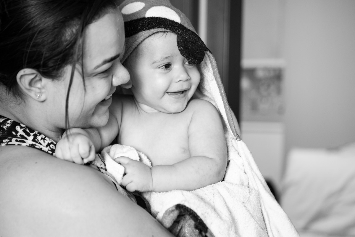 ensaio em familia em casa em salvador, menino no colo da mãe enrolado na toalha e rindo
