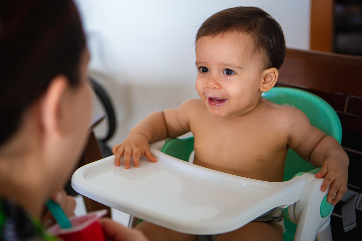 ensaio em familia em casa em salvador, criança sentada na cadeirinha olhando para a mãe e rindo