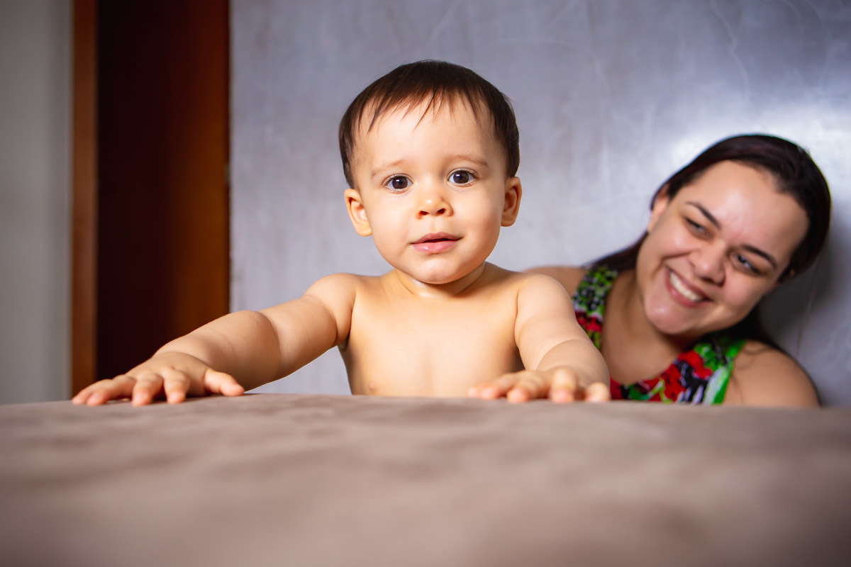 ensaio em familia em casa em salvador, criança em pé se segurando no sofá e mãe atrás sorrindo.