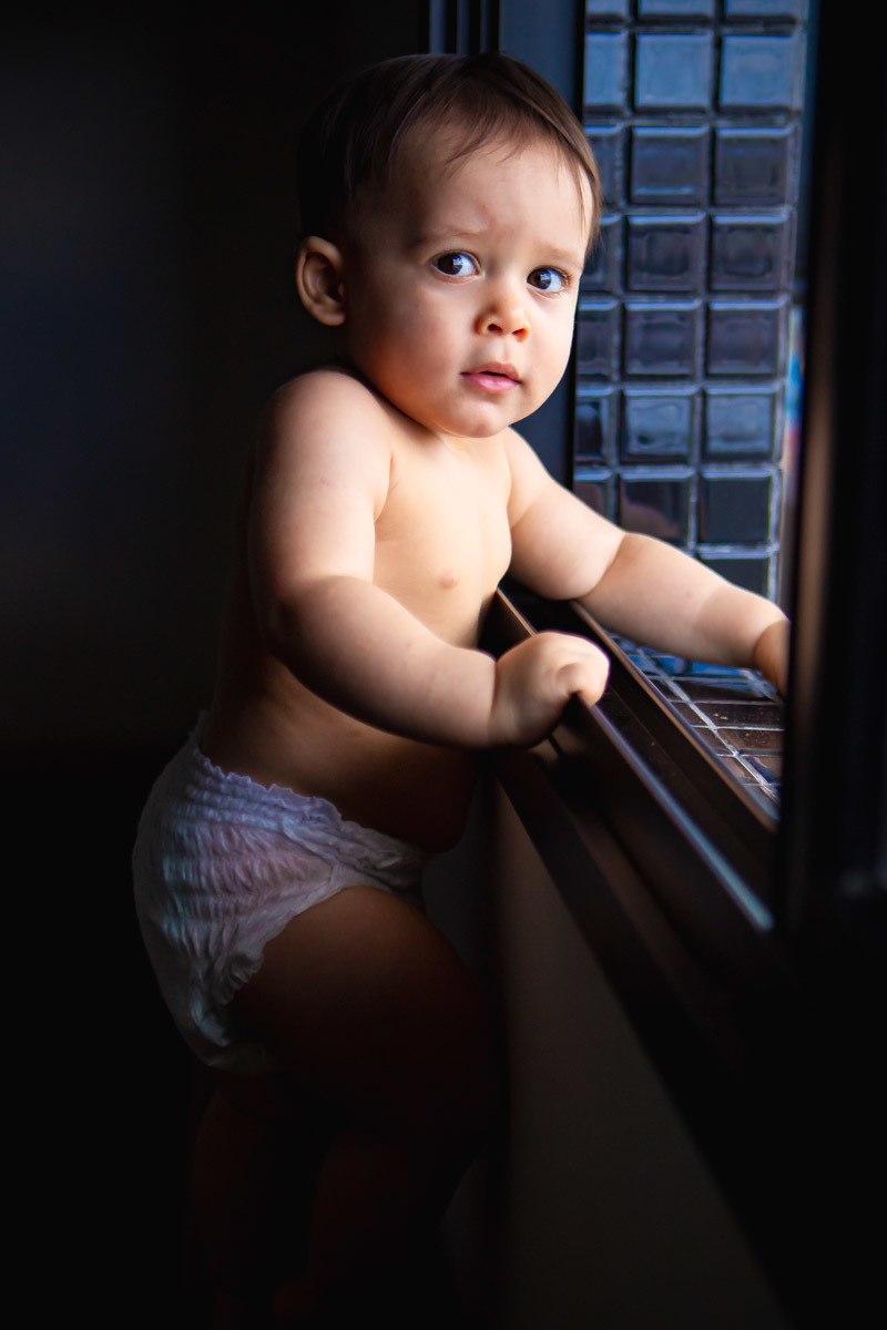 ensaio em familia em casa em salvador, criança em pé se segurando na janela.