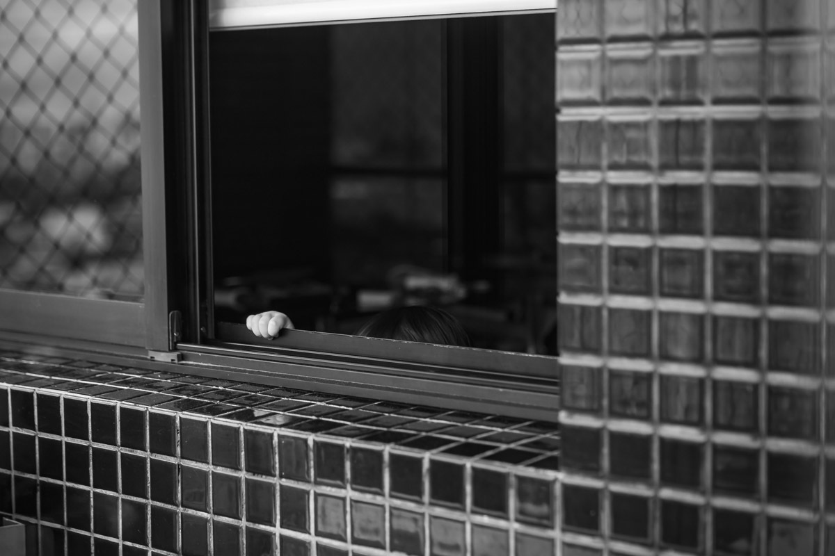 ensaio em familia em casa em salvador, menino brincando de se esconder e so mostrando a mão na janela.