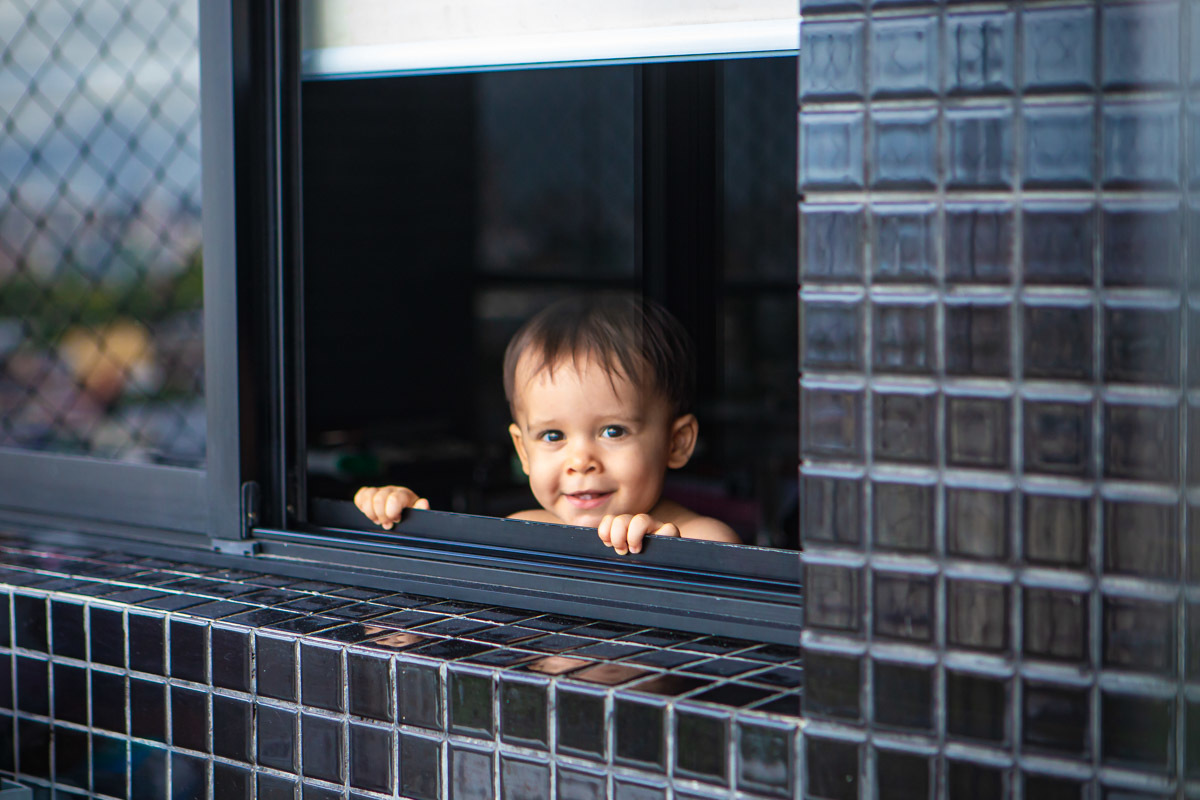 ensaio em familia em casa em salvador, menino brincando de se esconder e aparecendo na janela.