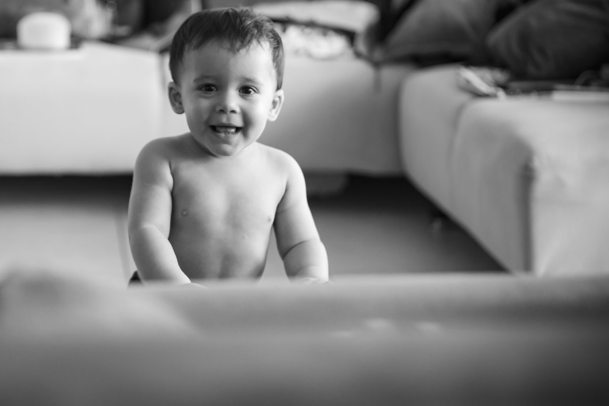 ensaio em familia em casa em salvador, menino brincando rindo em pé se segurando no sofá