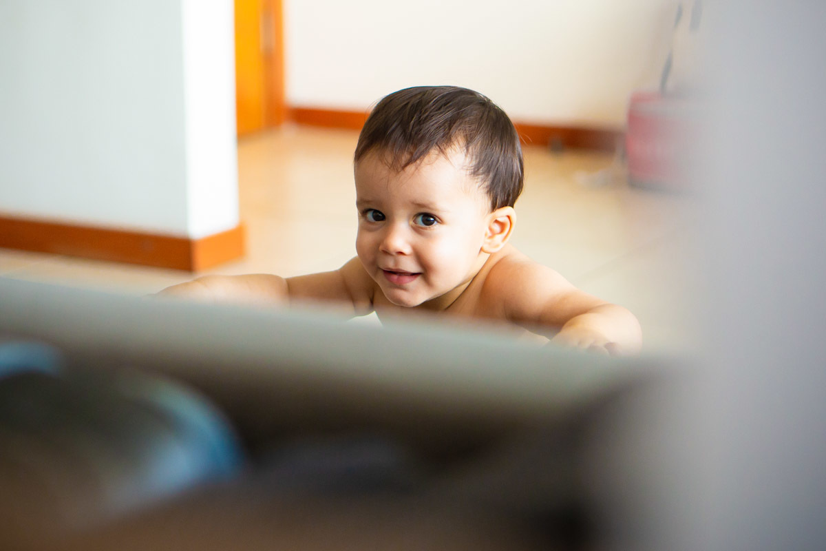 ensaio em familia em casa em salvador, menino brincando rindo em pé se segurando no sofá