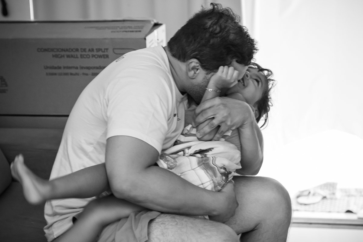 pai abraçando e beijando filha sentados no sofá