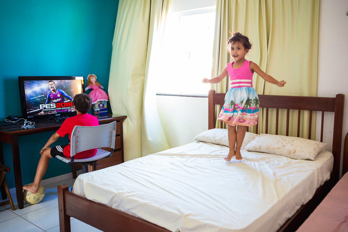 manina pulando na cama enquanto o irmão joga video game