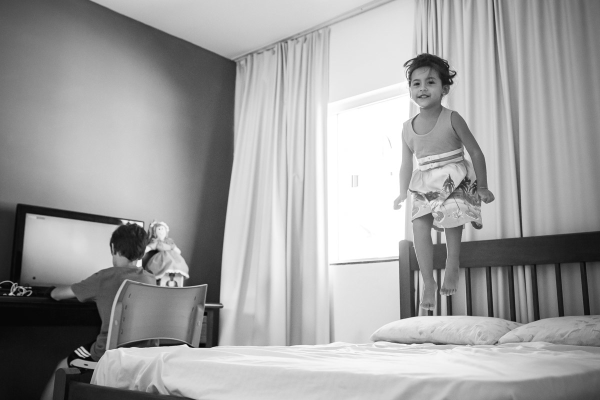 manina pulando na cama enquanto o irmão joga video game