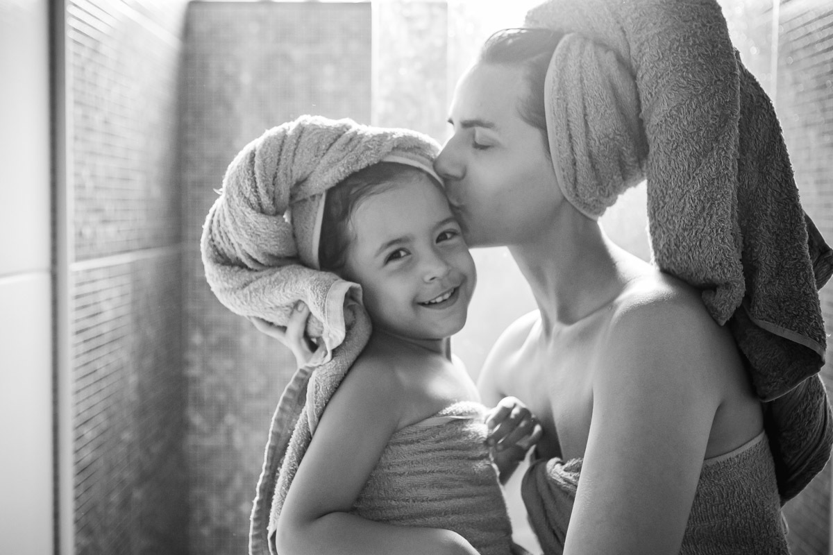 menina enrolada em toalha com toalha na cabeça e mãe beijando a sua cabeça.