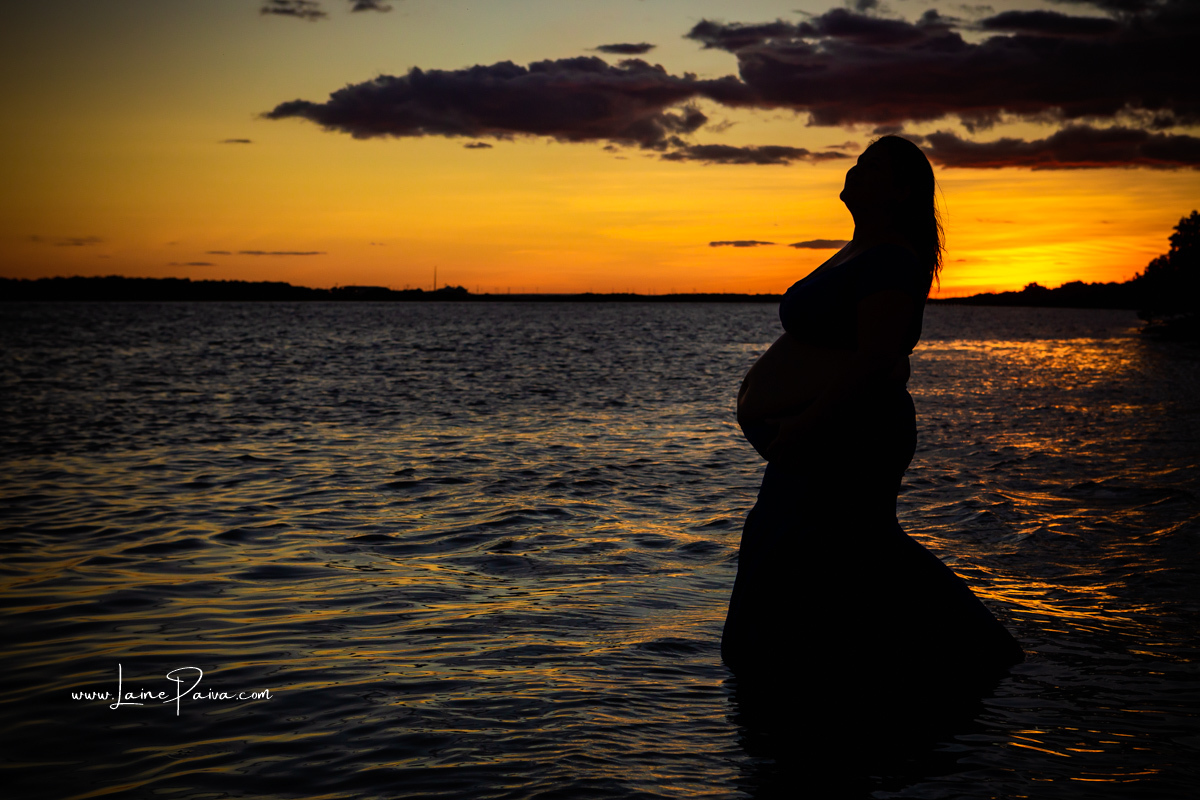 silhueta de gestante dentro de um rio  num ensaio no fim de  tarde num trapiche com um por do sol lindo.