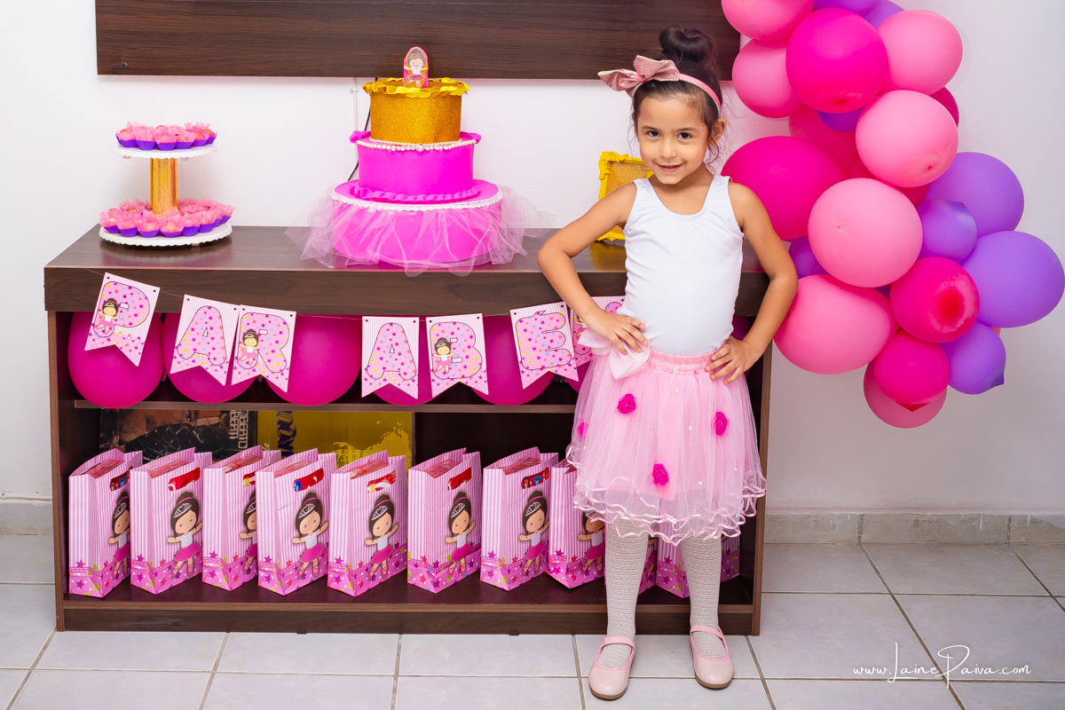menina com mão na cintura em frente a mesa e vestida de bailarina no seu aniversário.