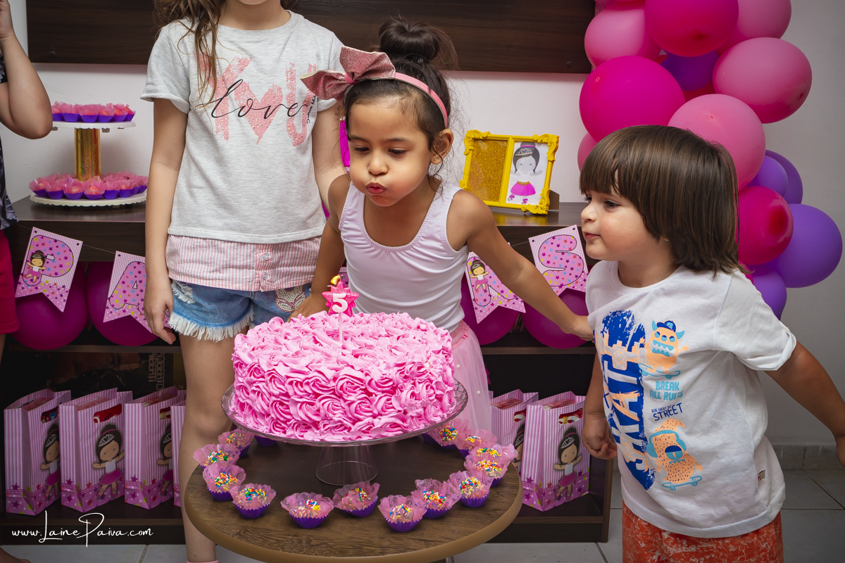 menina assoprando bolo de aniversário e primo mais novo do lado tentando assoprar também