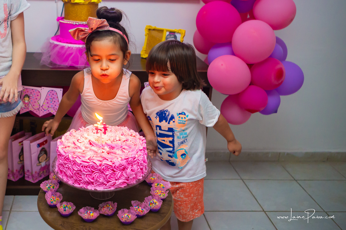 menina assoprando bolo de aniversário e primo mais novo do lado tentando assoprar também