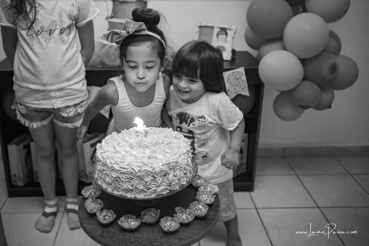 menina assoprando bolo de aniversário junto com primo mais novo que sorrir
