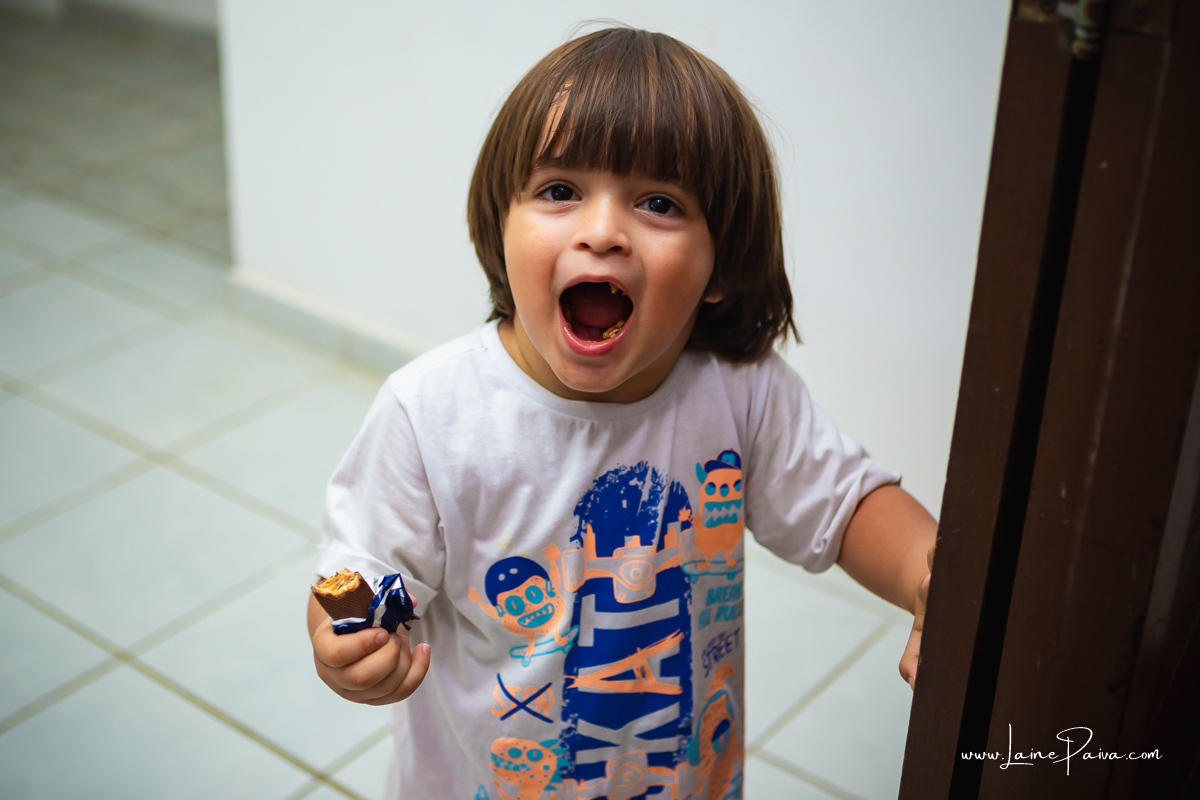 menino com chocolate na mão e boca aberta mostra o que ta comendo.