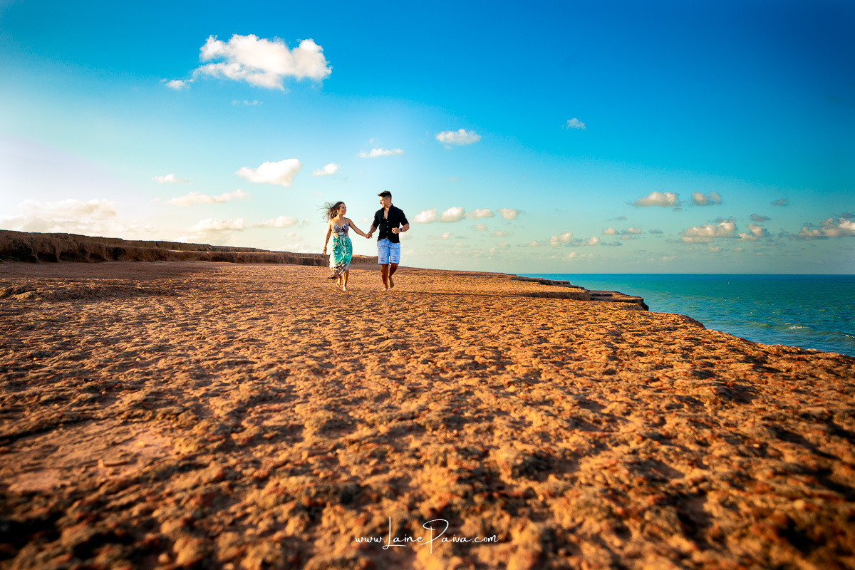 casal correndo de mãos dadas e se olhando no chapadão em Pipa