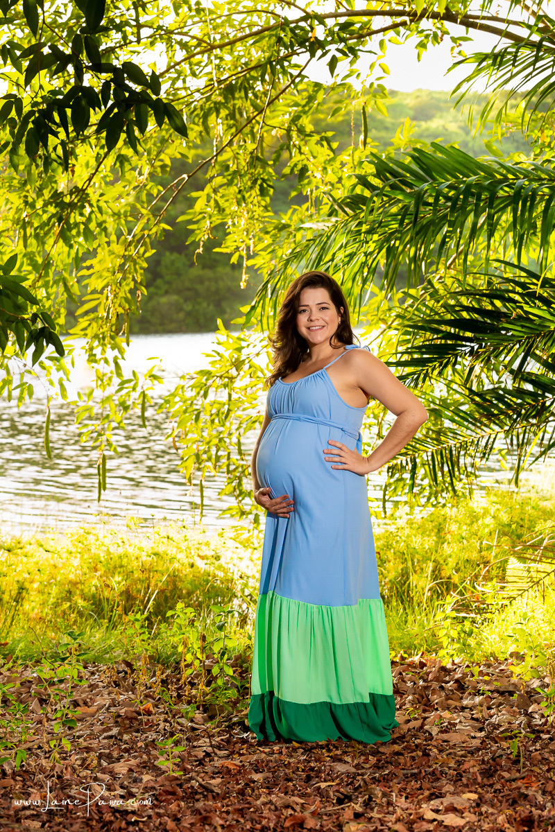 mulher com mão na cintura e a outras na barriga e sorrindo em ensaio gestante externo no sitio