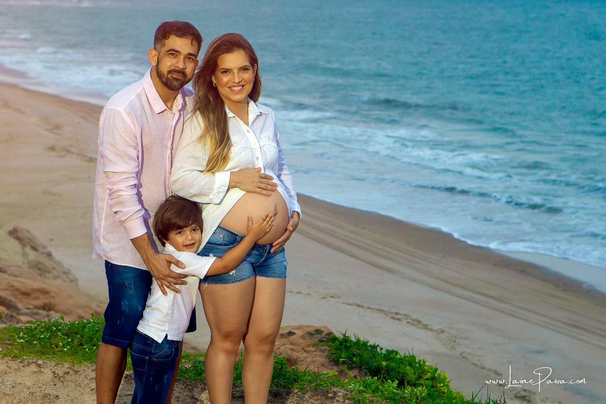 gestante sendo abraçada pelo marido e filho mais novo no ensaio gestante externo na praia na Árvore do amor.