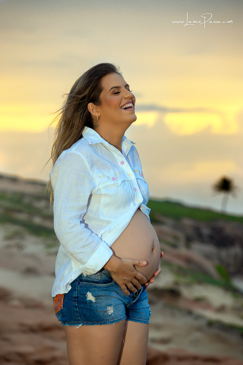 gravida com mão na barriga curtindo o fim de tarde no ensaio gestante externo na praia na Árvore do amor.