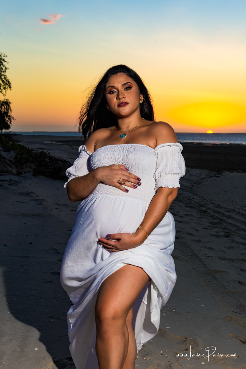 gravida  fazendo carinho em barriga com o sol se pondo no fundo em Chico Martins praia de Macau RN.