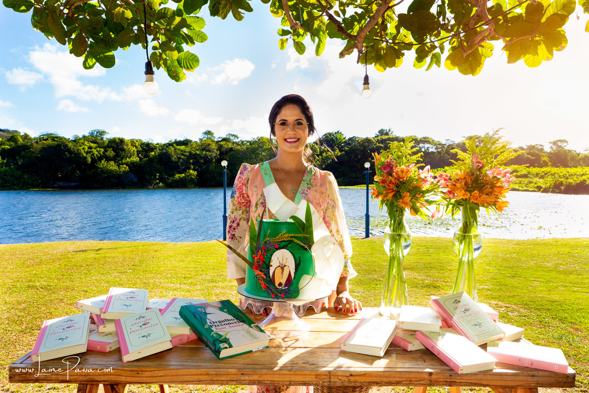 mulher com livro Orgulho e Preconceito mão em frente a mesa de bolo do seu aniversário de 40 anos na Chácara Bela Vista em Parnamirim/RN.