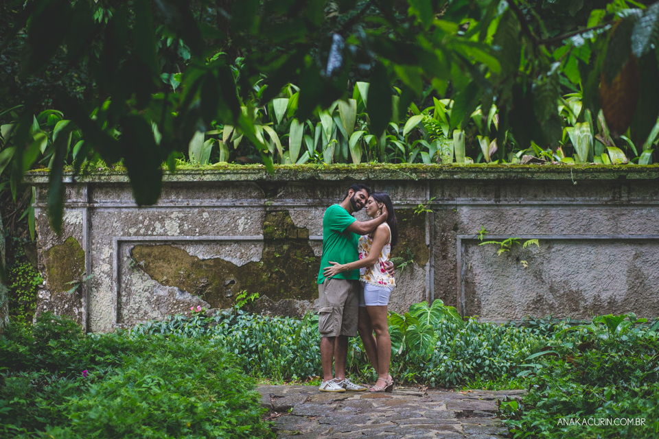 Casal de rosto colado, namorando, em pé em frente a uma parede de um muro antigo. Fotografia de casal feita por Ana Kacurin no Rio de Janeiro - RJ.
