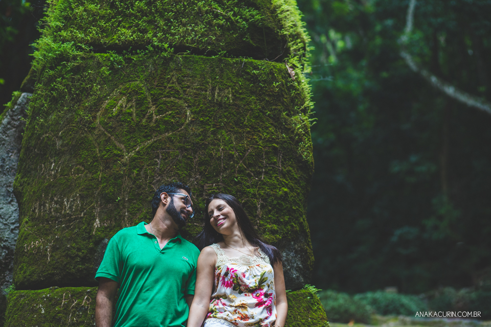 Casal de entreolhando,  recostado em torre de pedra coberta de musgo verdinho. Fotografia de casal feita por Ana Kacurin no Rio de Janeiro - RJ.