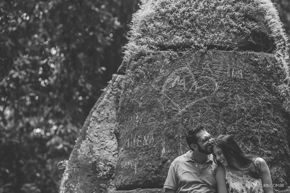 Casal de entreolhando,  recostado em torre de pedra coberta de musgo em preto e branco. Fotografia de casal feita por Ana Kacurin no Rio de Janeiro - RJ.