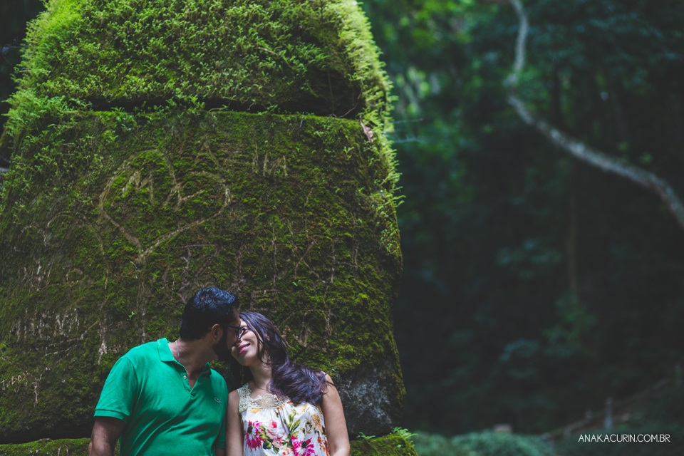 Casal de entreolhando,  recostado em torre de pedra coberta de musgo verdinho. Fotografia de casal feita por Ana Kacurin no Rio de Janeiro - RJ.