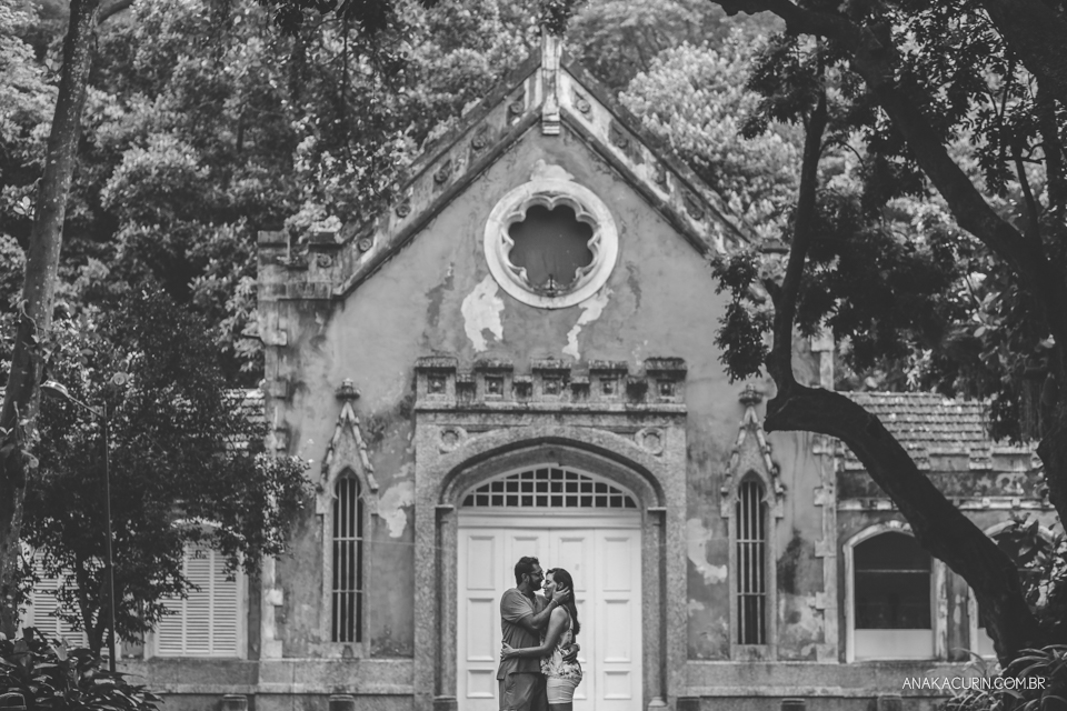 Casal se abraça ao longe, em frente a uma bela  e majestosa construção antiga. Fotografia de casal feita por Ana Kacurin no Rio de Janeiro - RJ.