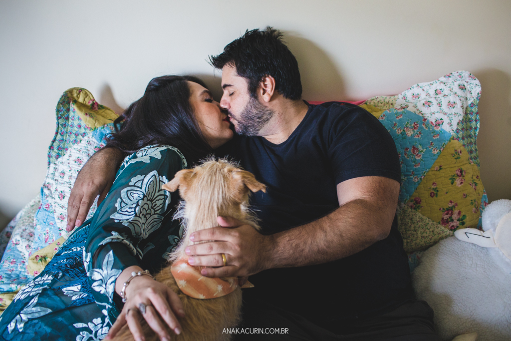 Gestante Flávia e Fábio deitados na cama, namorando com o pet cão Simba ao lado