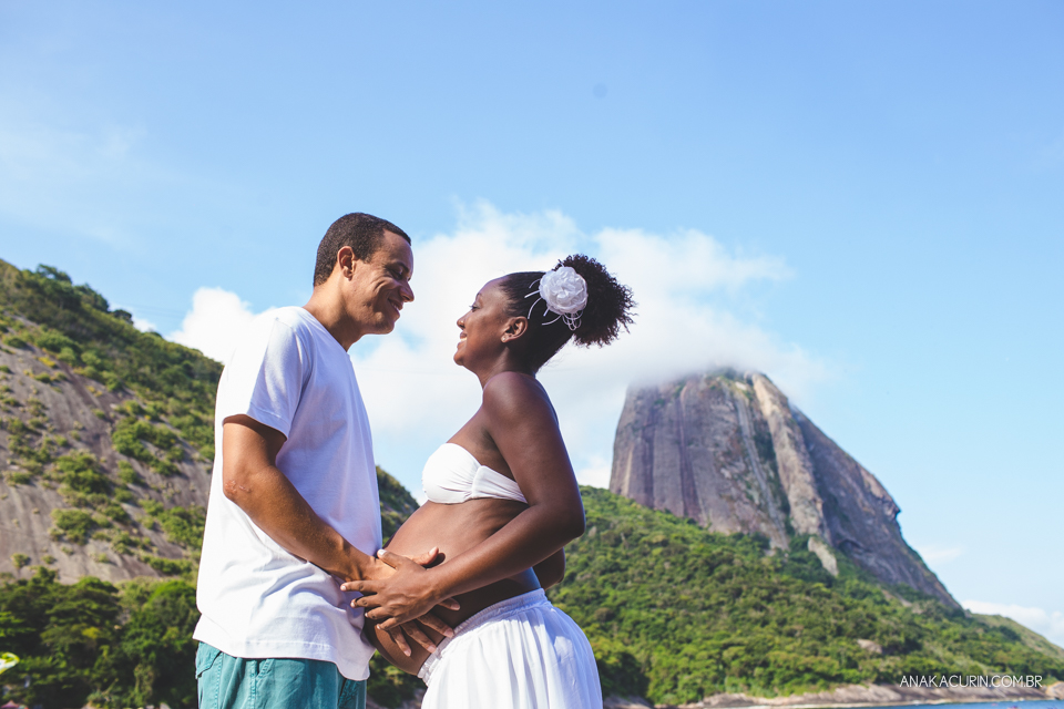 Casal grávido se olhando com o Pão de Açúcar ao fundo, no Rio de Janeiro