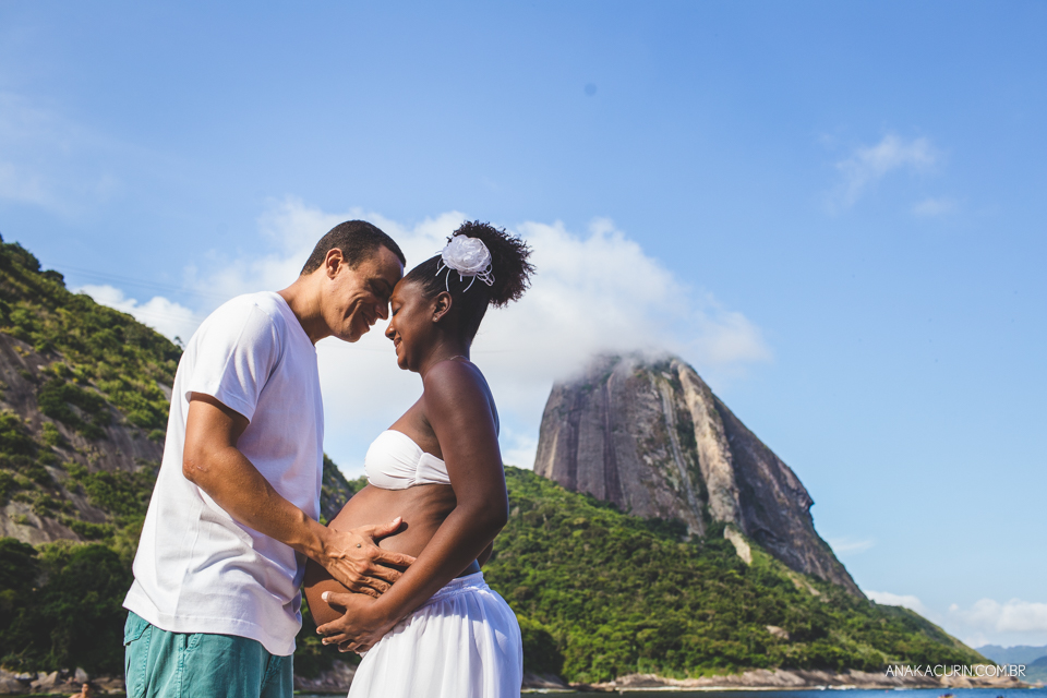 Casal grávido se olhando com o Pão de Açúcar ao fundo, no Rio de Janeiro