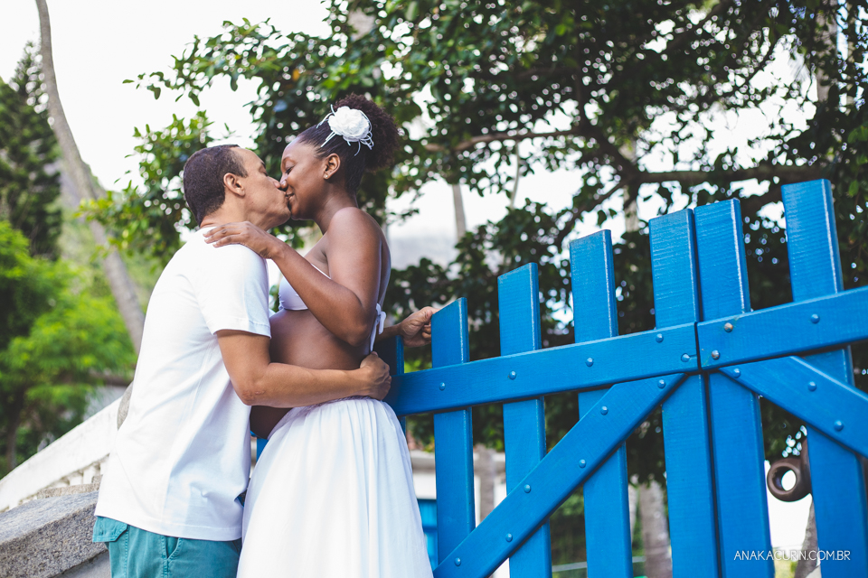 Casal grávido se entreolhando e sorrindo ao topo de uma escadaria com um portão azul ao fundo