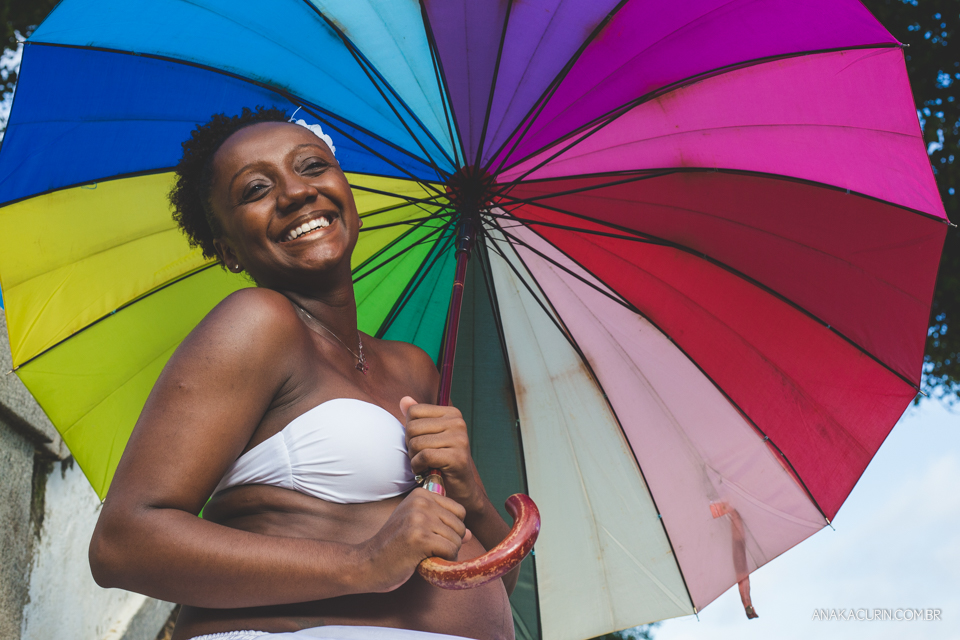 Grávida sorrindo segura uma sombrinha com as cores do arco-íris