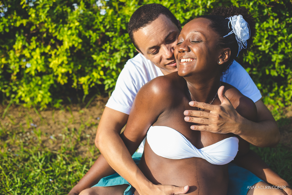 Casal grávido sentado na grama se abraçando