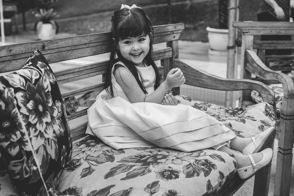 Daminha sorrindo sentada em banco de madeira