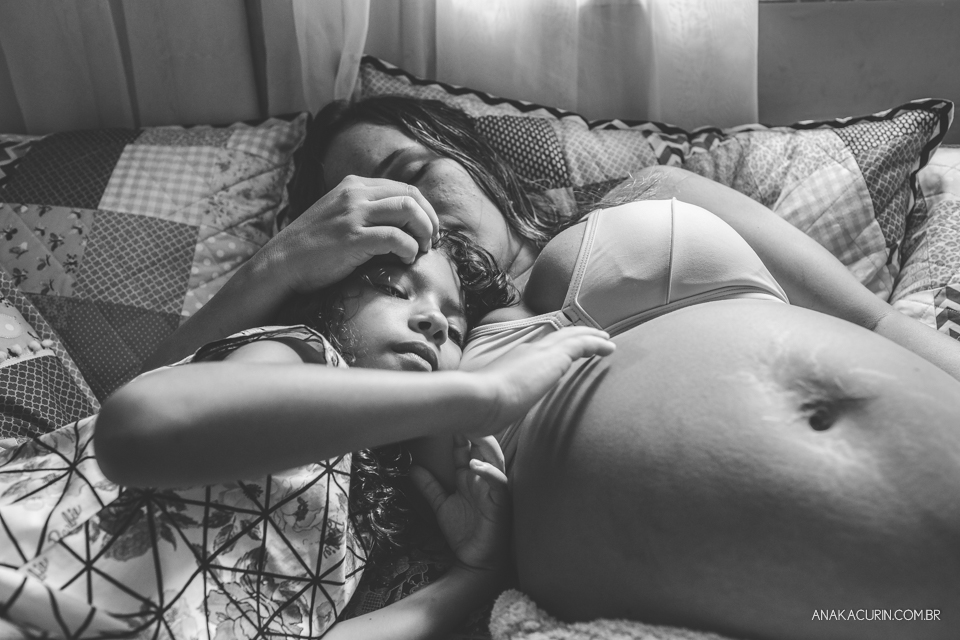 Gestante em trabalho de parto em um quarto de criança em sua casa sendo amorosamente assistida pelas duas filhas pequenas