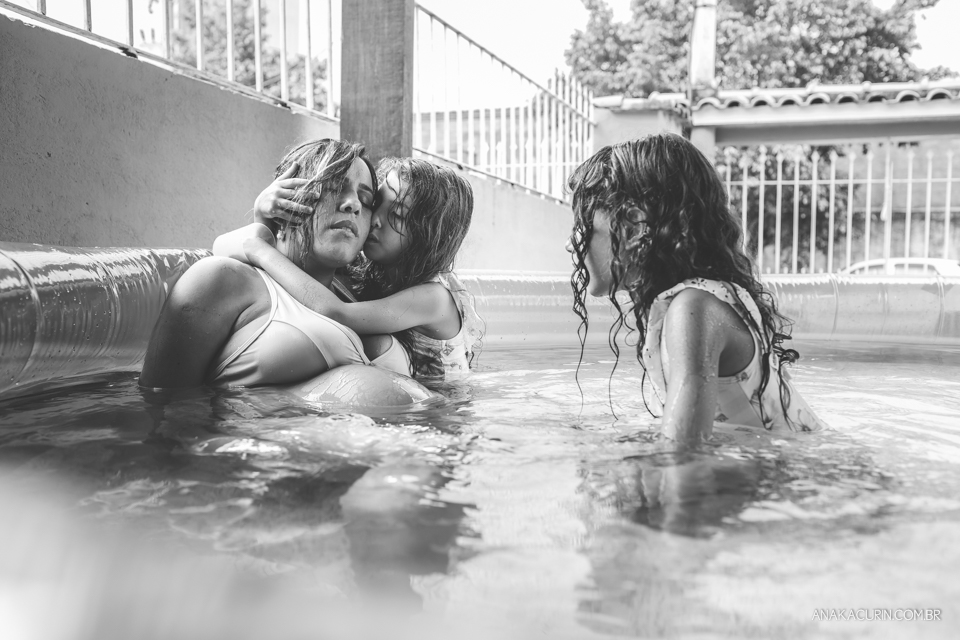 Gestante em trabalho de parto em casa, numa piscina no quintal sendo amorosamente assistida pelas duas filhas pequenas