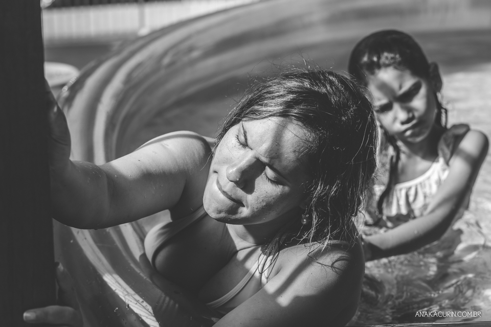 Gestante em trabalho de parto em casa, numa piscina no quintal sendo amorosamente massageada por uma de suas filhas