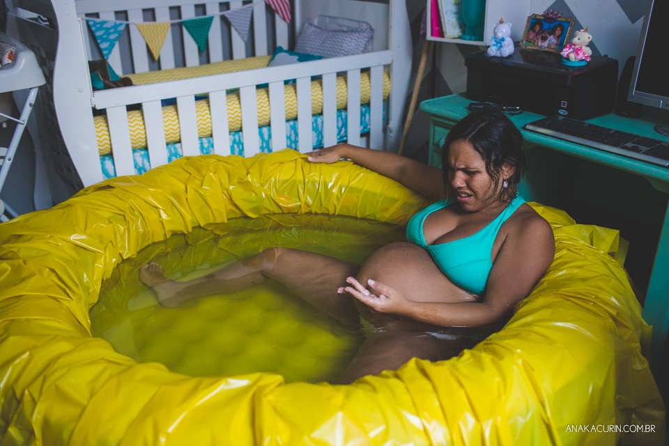 Gestante em trabalho de aprto em casa, mergulhada numa piscina amarela olha com espanto o tampão mucoso que acabou de sair em sua mão