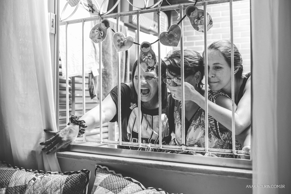 Família de gestante espiando pela janela de casa o trabalho de parto com expressões de felicidade e ansiedade.