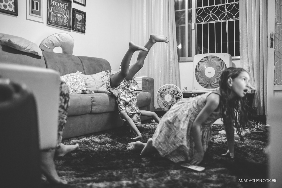 crianças brincando na sala enquanto a mãe está em trabalho de parto em casa. Uma delas está de ponta-cabeça no sofá.