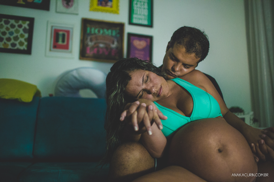 Gestante em trabalho de parto em casa sentada na banqueta de parto com descansando, sendo amorosamente sustentada pelo marido.