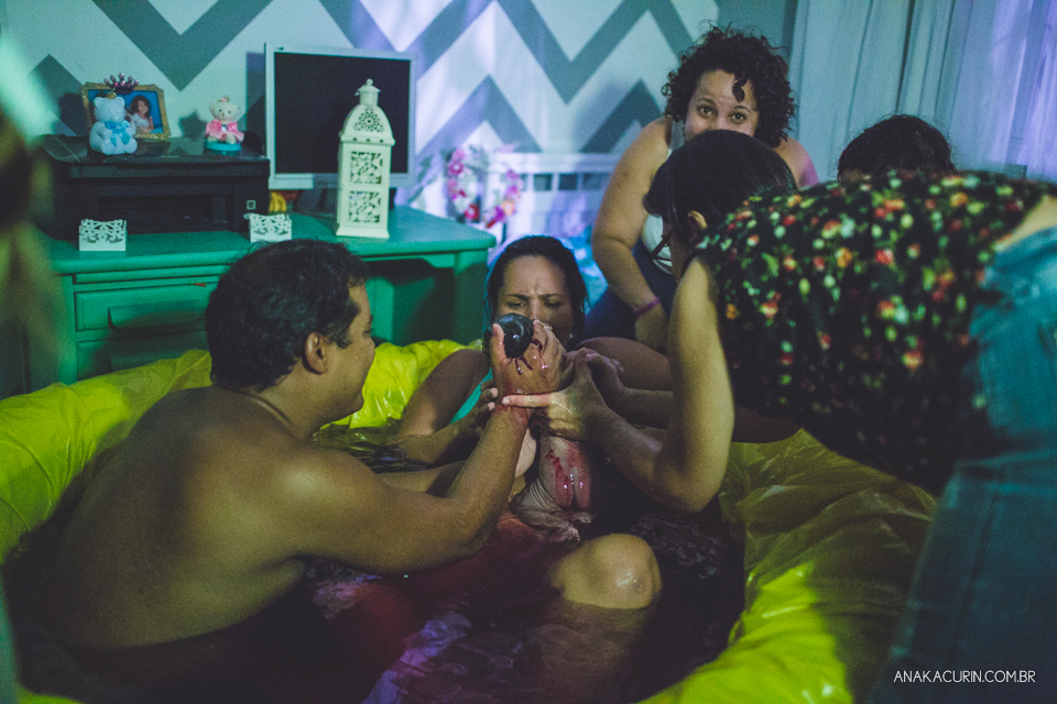 Pai entrega o bebê recém nascido para a ma~e recém parida na piscina de casa