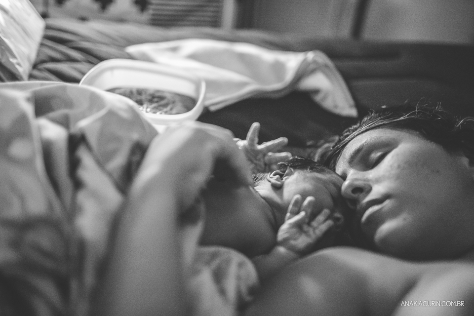 Mulher deitada ao lado de bebê recém parido emcostando rosto com rosto.