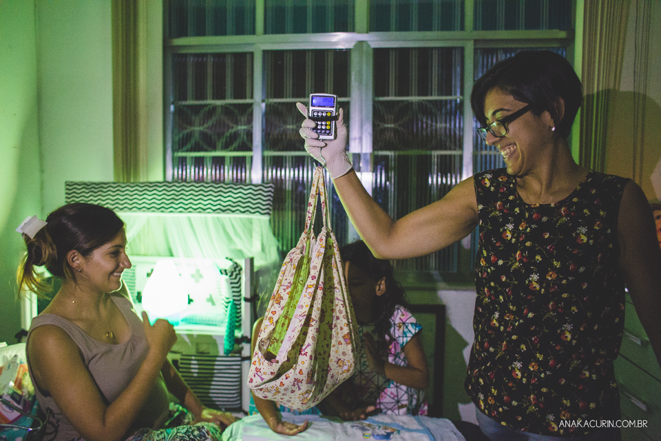 PArteira pesa bebê recém nascido em balança de mão, no quarto do casal.